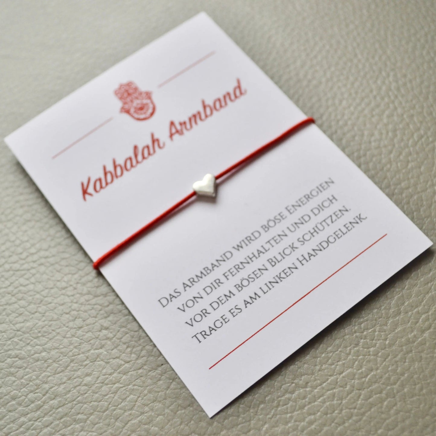 Kabbalah Armband mit silbernem Herz und rotem Band auf Schmuckkarte – handgefertigtes Schutzarmband gegen den bösen Blick als liebevolles Geschenk.