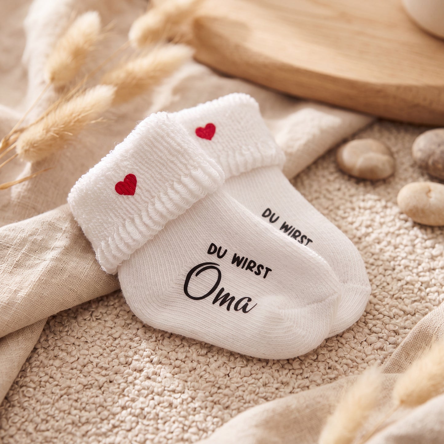 Personalisierte Babysocken „Du wirst Oma“ und „Du wirst Opa“ mit roten Herzen in einem natürlichen beigefarbenen Geschenk-Setting.