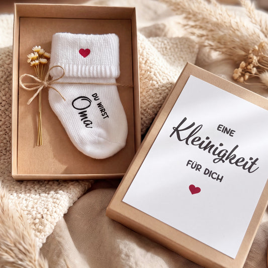Personalisierte Babysocke „Du wirst Oma“ mit rotem Herz in einer Geschenkbox – besondere Idee zur Schwangerschaftsverkündung für werdende Großeltern.