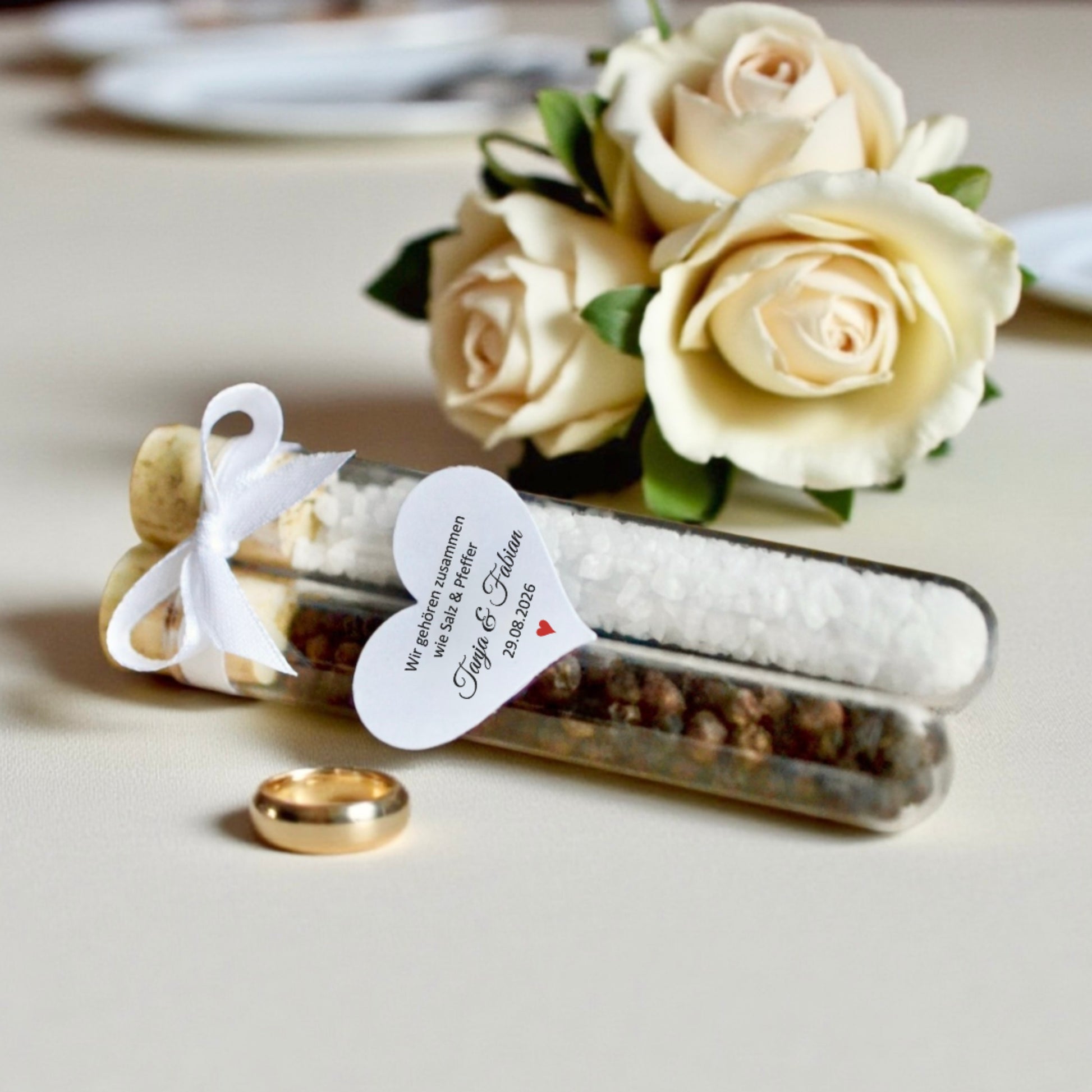 Hochzeitsgastgeschenk aus Acrylglas mit Salz und Pfeffer, dekoriert mit weißer Schleife und personalisiertem Herz-Anhänger, elegante Geschenkidee und Tischdekoration für Hochzeit in romantischem Stil.