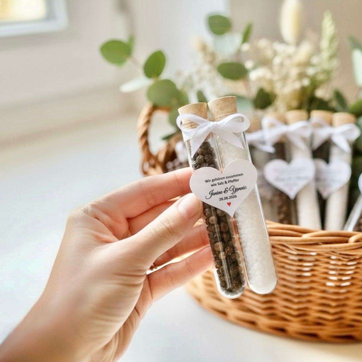Personalisiertes Hochzeitsgastgeschenk im Reagenzglas mit Salz und Pfeffer, gehalten in der Hand vor dekorativem Korb