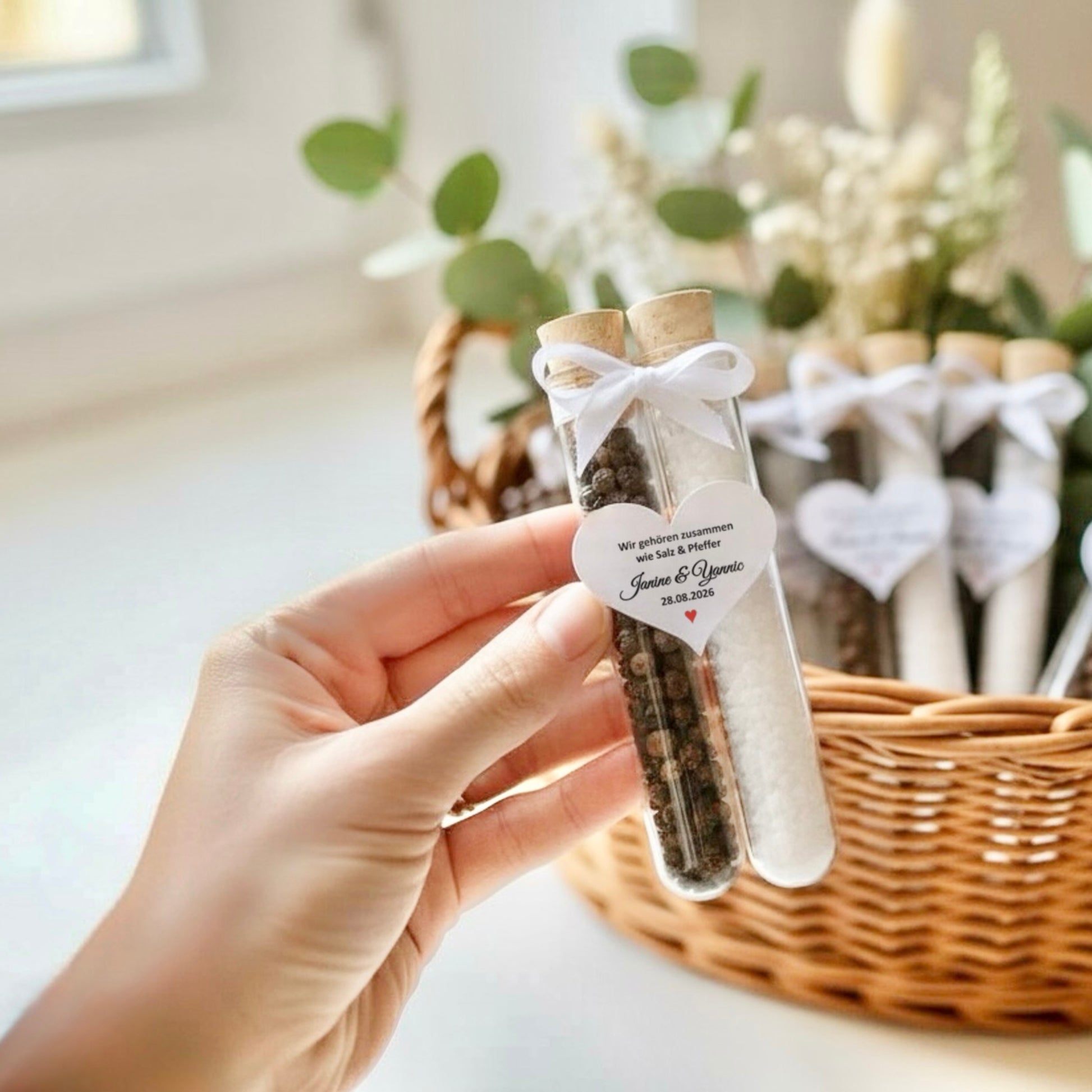 Personalisiertes Hochzeitsgastgeschenk im Reagenzglas mit Salz und Pfeffer, gehalten in der Hand vor dekorativem Korb